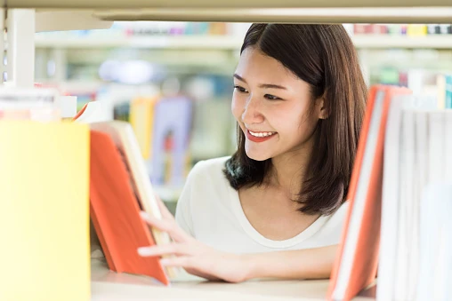 Estudante sorrindo enquanto escolhe um livro na estante de uma biblioteca