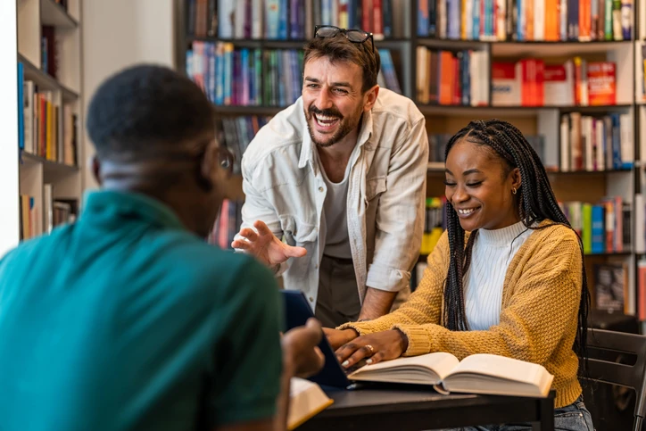 Professor e alunos estudando juntos em uma biblioteca com estantes de livros