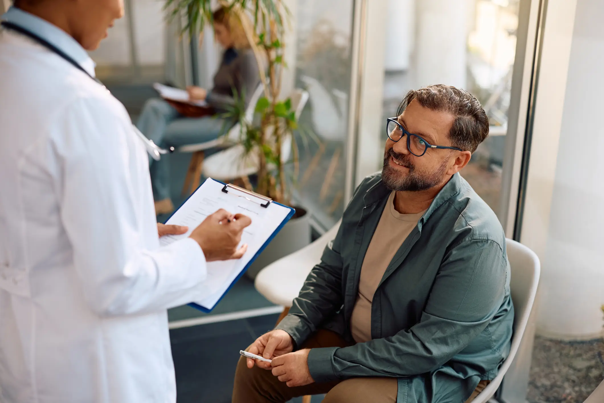 Atendimento médico humanizado: médica preenchendo prontuário enquanto conversa com paciente em consultório