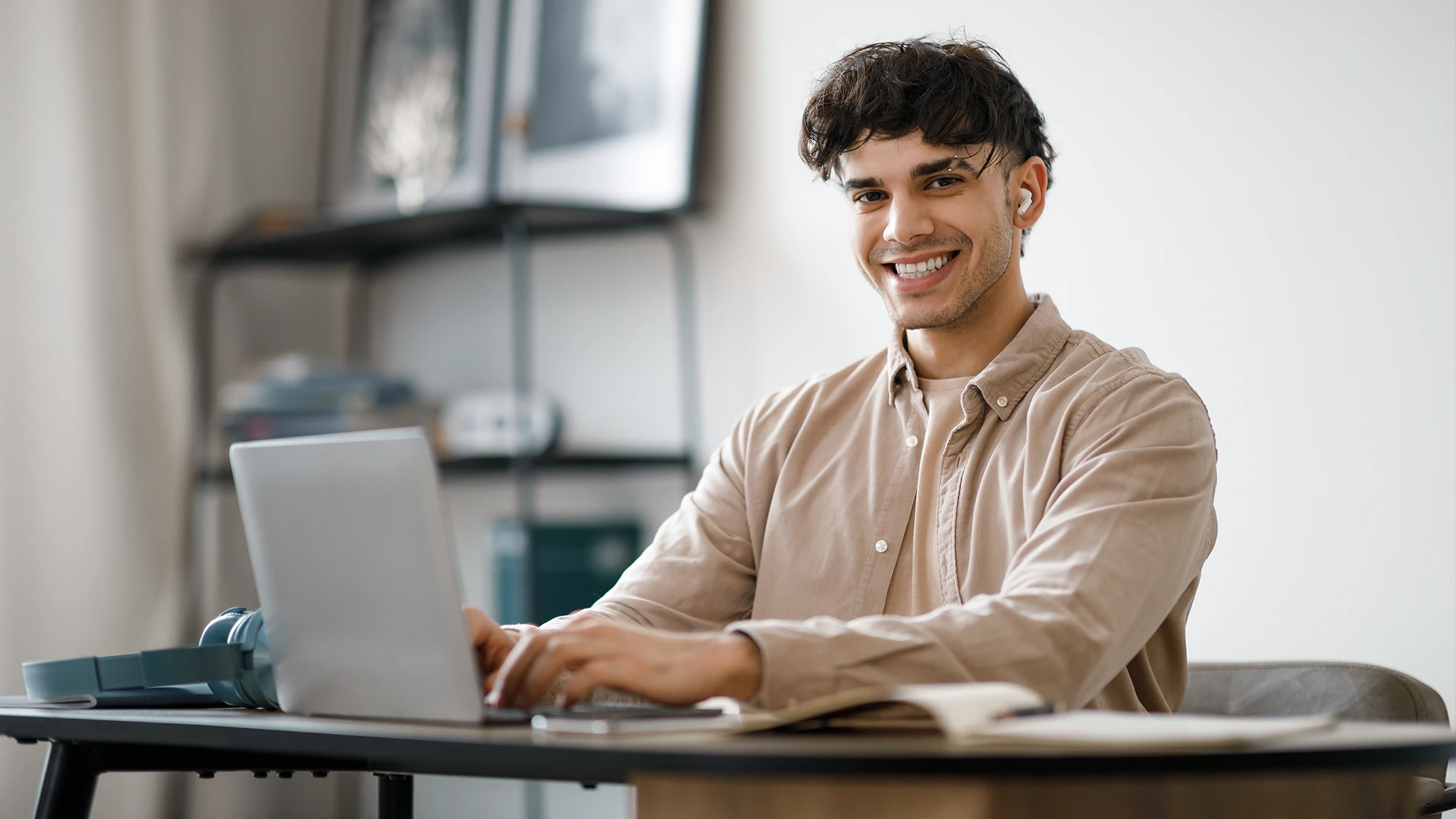 Jovem estudante ou profissional sorrindo enquanto usa notebook em home office