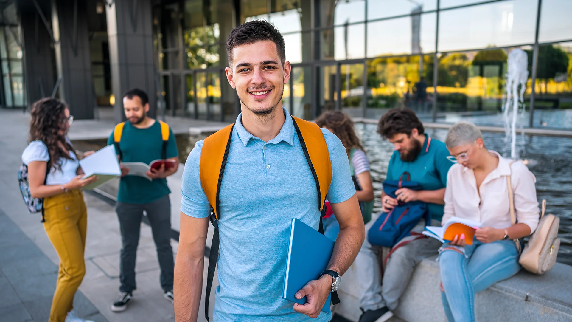 Estudante universitário sorridente segurando livros com colegas ao fundo no campus