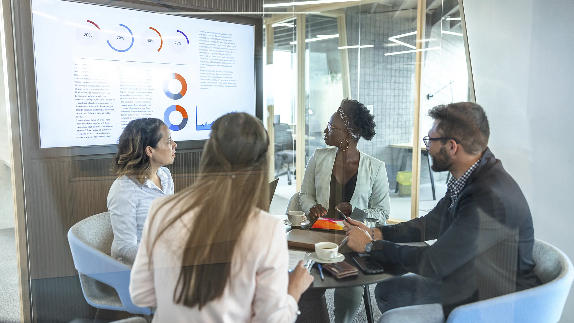 Equipe diversa reunida em uma sala de reuniões corporativa analisando gráficos de dados em uma tela digital.